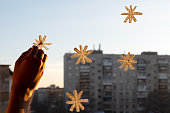 A woman's hand draws snowflakes on the window with paint, everything is illuminated by a soft yellow sunset light
