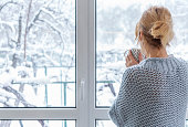 A woman looks out of the window at the snow-covered outdoors