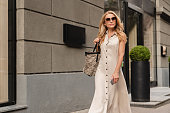 Middle-aged mature woman with blond hair wearing sunglasses walking on city streets while doing shopping outdoors. Sales and discounts concept.