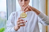 Close-up of glass of water with lemon in hands of young female