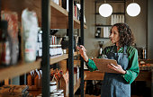 Mature deli owner taking inventory on store shelves using a clipboard