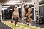 Strong fit sportswoman doing lunges with dumbbells at gym with her trainer.