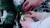 Festive and elegant, a family adorns a christmas tree with white ornaments and string lights. A day with family before Christmas. New Year's Eve with family