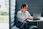Focused Professional Woman Working on Laptop in a Modern Office Booth