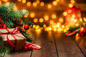 Christmas present wrapped with craft paper and red ribbon under the Christmas tree in a cozy festive atmosphere with defocused Christmas lights at background