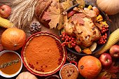 Traditional Thanksgiving still life. Roasted turkey, pumpkin pie, cranberries, autumn pumpkins and nuts on a dark wooden table. Top view. Holiday concept
