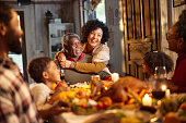 Happy black grandparents talking to their family during lunch on Thanksgiving.