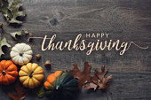 Happy Thanksgiving calligraphy text with fall pumpkins, squash and leaves over dark wood background